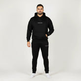 Celvian Distinctive black tracksuit, front view showcasing embroidered logos on hoodie and pants, relaxed athletic fit, studio lighting.