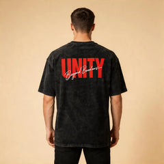 Male model wearing the Celvian Beyond Borders T-Shirt in washed black, shown from the back with the bold red UNITY and white Beyond Borders graphic on a beige studio background.