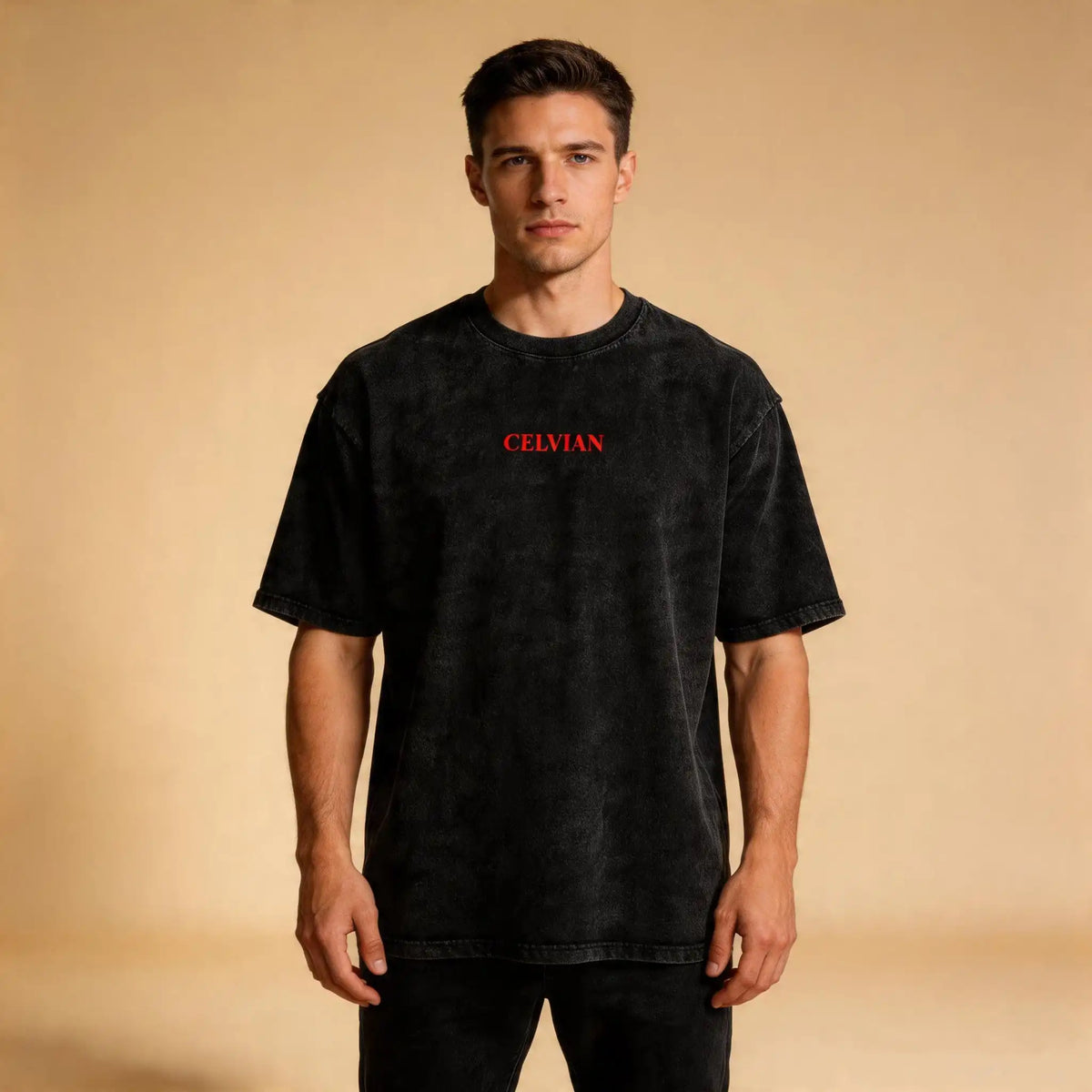 Male model wearing the Celvian Beyond Borders T-Shirt in washed black, shown from the front with a minimal red CELVIAN chest logo on a beige studio background.