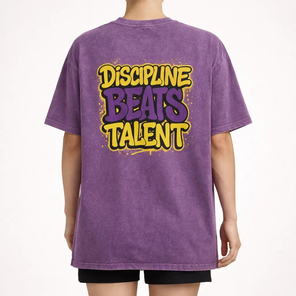 Back view of purple acid-wash oversized t-shirt with large ‘Discipline Beats Talent’ graphic print.