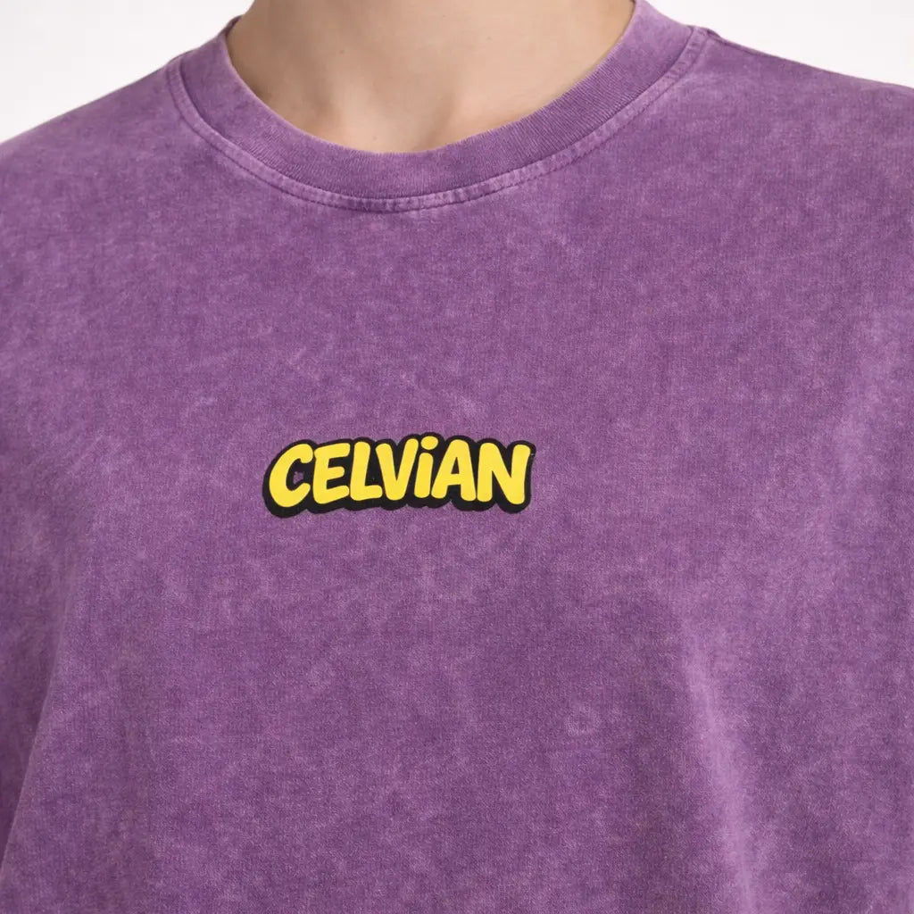 Close-up of purple washed t-shirt showing small yellow Celvian chest logo and crew neck collar.