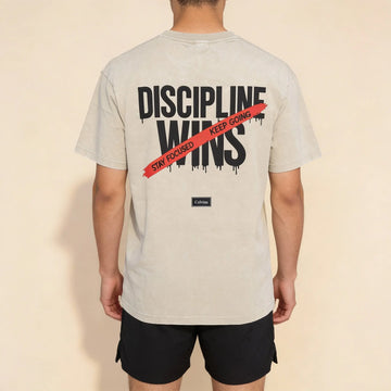 Back view of beige oversized t-shirt with ‘Discipline Wins’ print and red ‘Stay focused, keep going’ stripe, Celvian label.