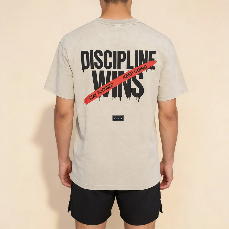 Back view of beige oversized t-shirt with ‘Discipline Wins’ print and red ‘Stay focused, keep going’ stripe, Celvian label.