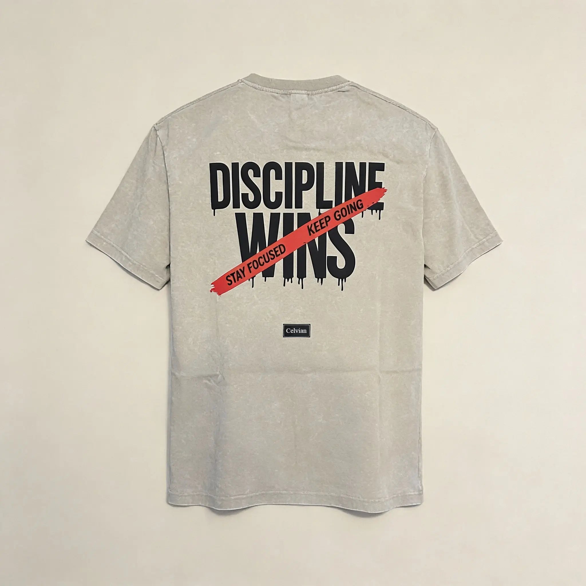 Back view of beige washed t-shirt featuring ‘Discipline Wins’ graphic with red ‘Stay focused, keep going’ stripe and Celvian label.
