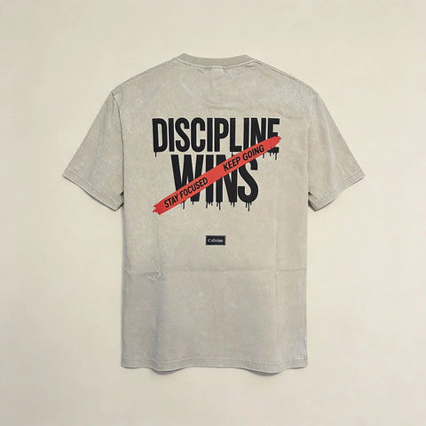 Back view of beige washed t-shirt featuring ‘Discipline Wins’ graphic with red ‘Stay focused, keep going’ stripe and Celvian label.