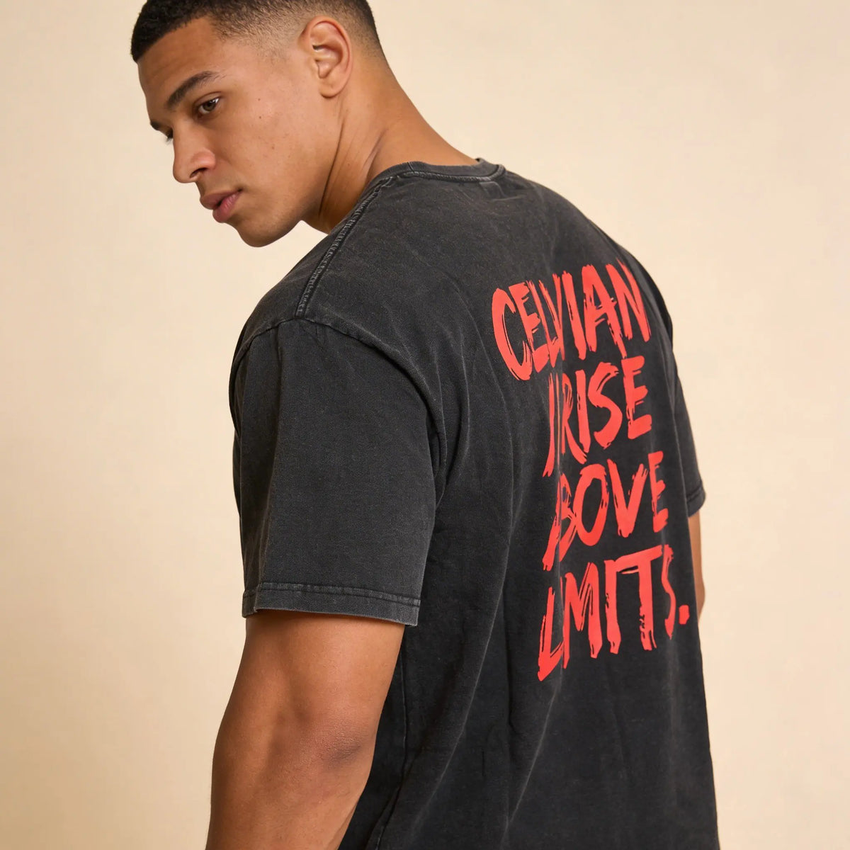 Back angled view of a man wearing the Celvian No Limits T-Shirt in washed black, featuring the bold red ‘CELVIAN // RISE ABOVE LIMITS.’ back graphic and oversized fit.