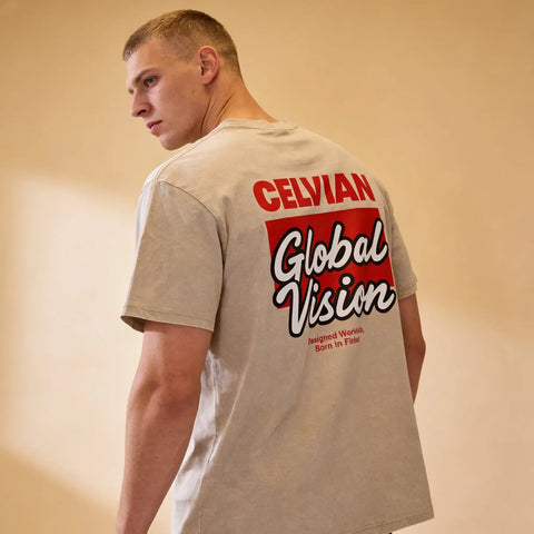 Male model wearing the Celvian Sandstone Global Vision T-Shirt in a washed beige finish, shown from a back angled view with the bold Global Vision graphic.