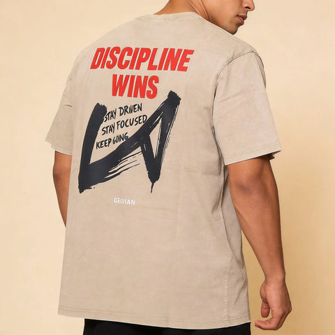 Back detail of male model wearing the Celvian Stay Driven oversized T-shirt in sandstone, featuring the red “Discipline Wins” graphic and bold brushstroke back print.